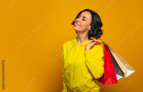 Can't wait to wear new clothes! Half-length photo of a young woman, turned sideways, caring her purchase in colorful bags behind her shoulder and dreaming about her new clothes.