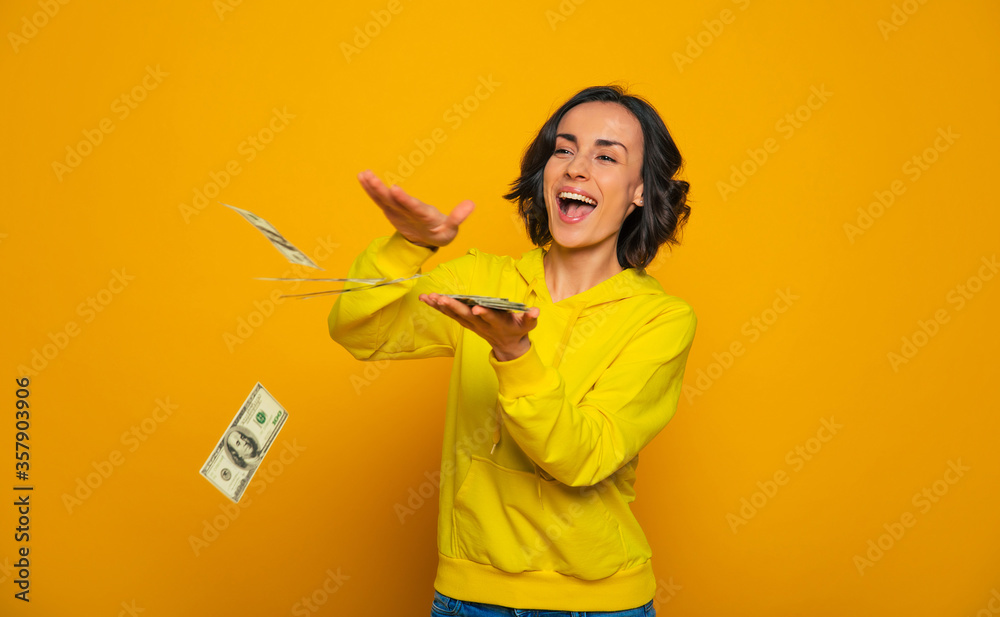 Success! Half-length photo of successful young woman in a yellow hoodie, laughing and throwing her money. Success! Half-length photo of successful young woman in a yellow hoodie, laughing and throwing her money.