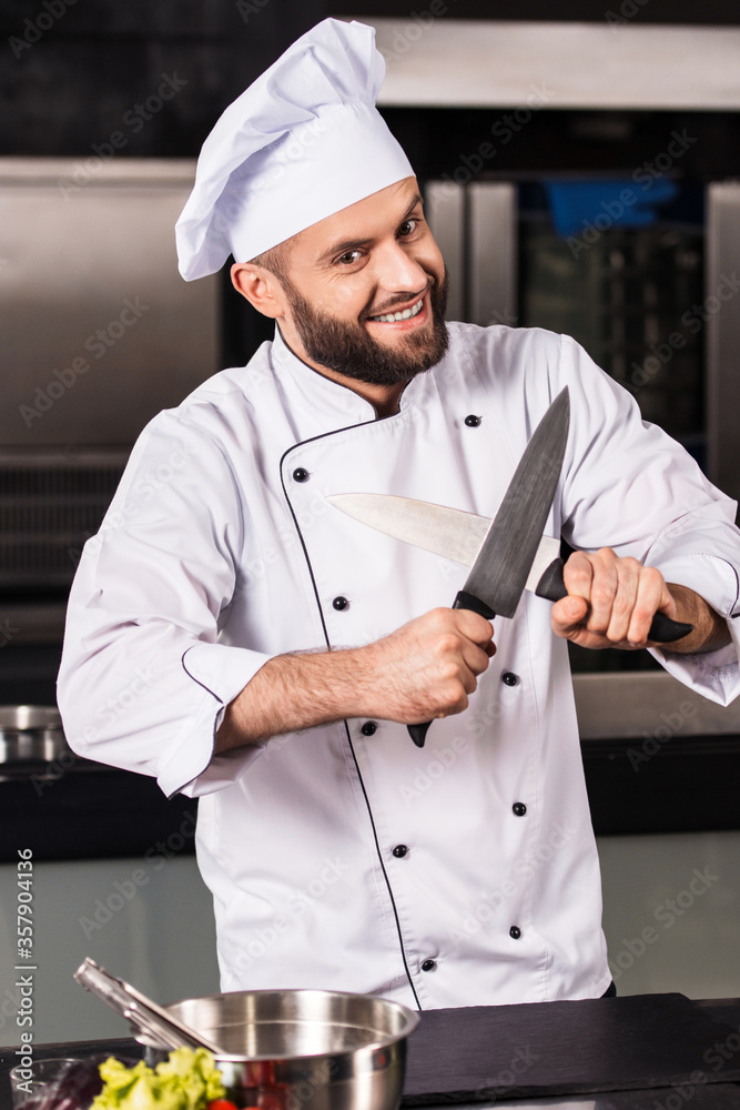 Professional chef posing at restaurant kitchen. Smiling male cook with crossed knives.