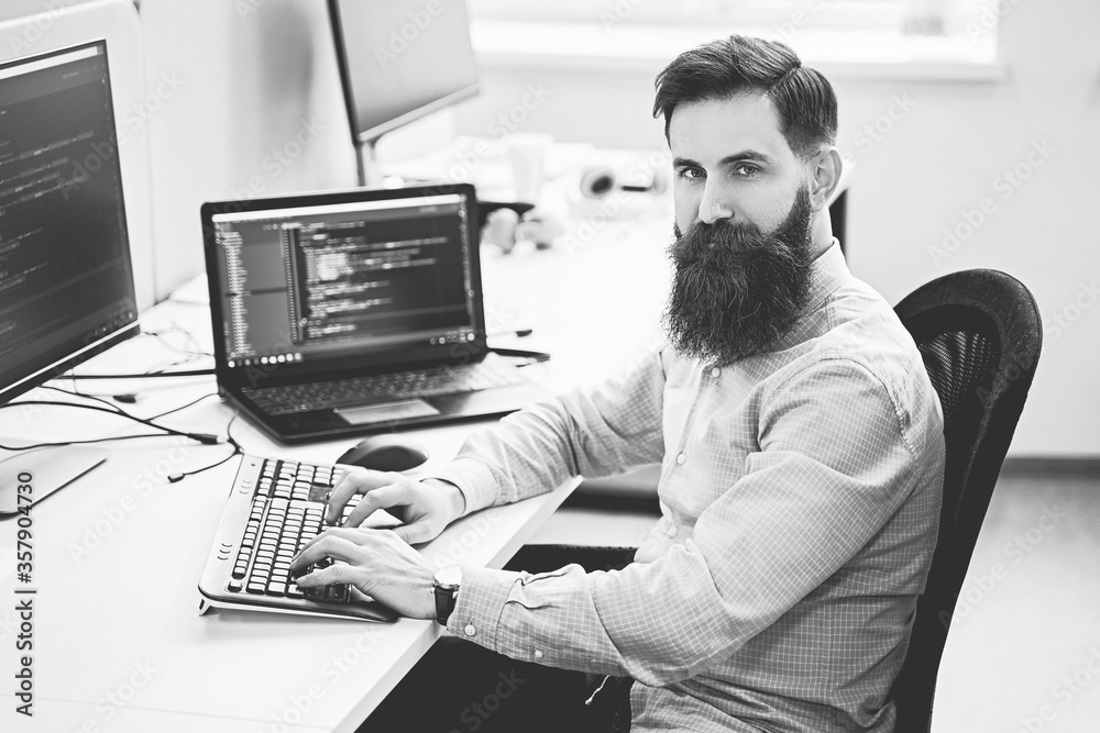 Serious computer programmer developer working in IT office, sitting at desk and coding, working on a project in software development company or startup. Black and white,