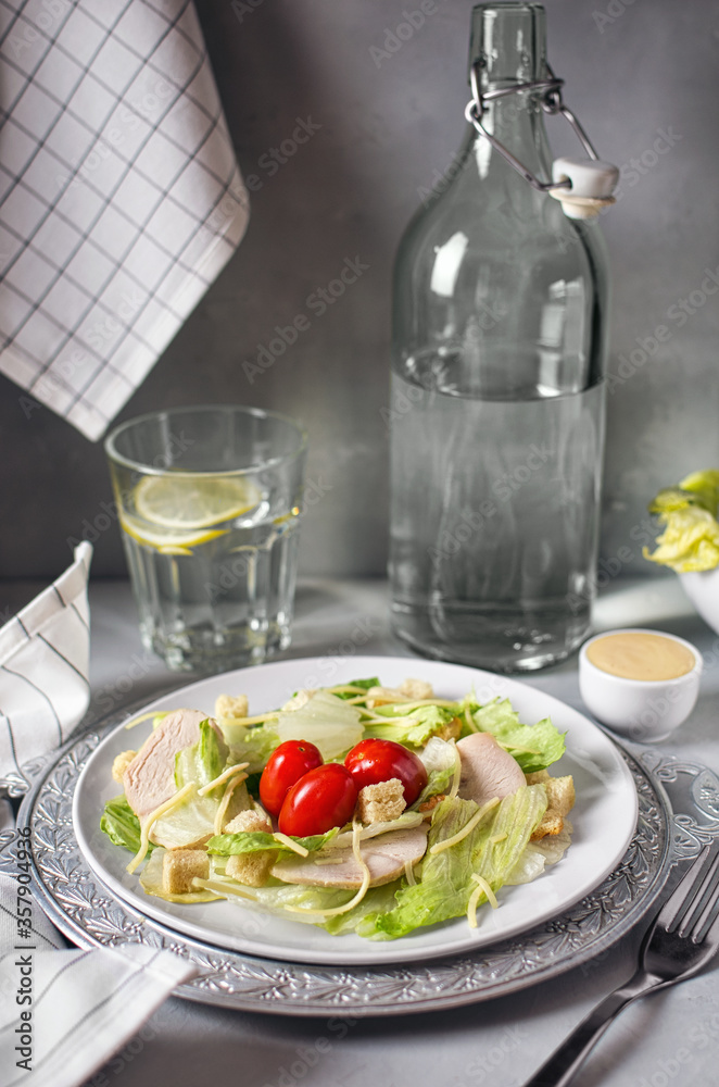 Delicious fresh Caesar salad with chicken on a gray stone background, delicious low-calorie diet, light snack Caesar salad and a glass of water