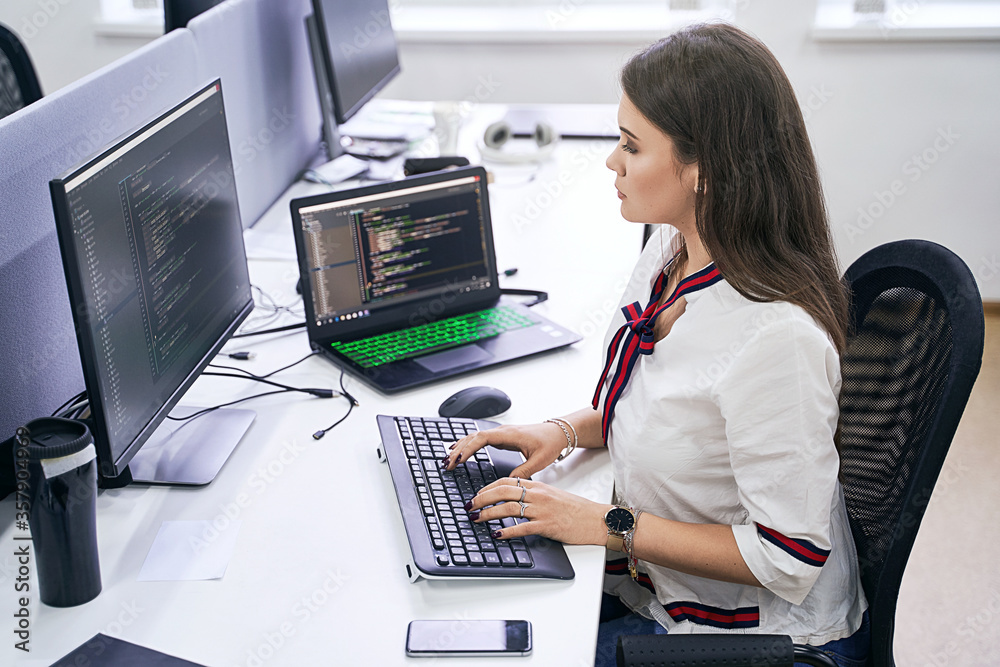 Beautiful female junior software developer working on computer in IT office, sitting at desk and coding, working on a project in software development company or technology startup. High quality image. Beautiful female junior software developer working on computer in IT office, sitting at desk and coding, working on a project in software development company or technology startup. High quality image.