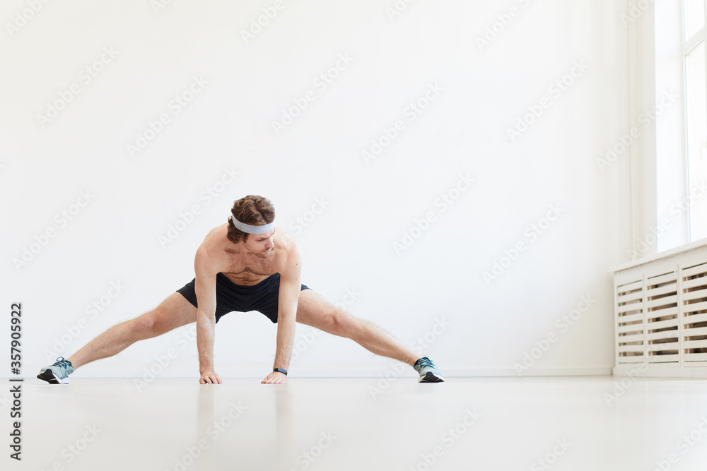 Shirtless muscular man doing stretching exercises during sports training