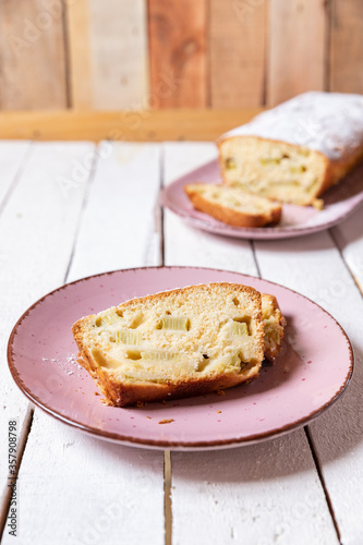 geschnittener, frischer Kuchen mit Rhabarber, Puderzucker und Eierlikör auf einem Tisch aus Holz in der Küche am Nachmittag