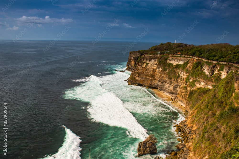 A beautiful landscape of costal area with cloud in sky and green water pounding on the stone surface during the touristic visit in Bali