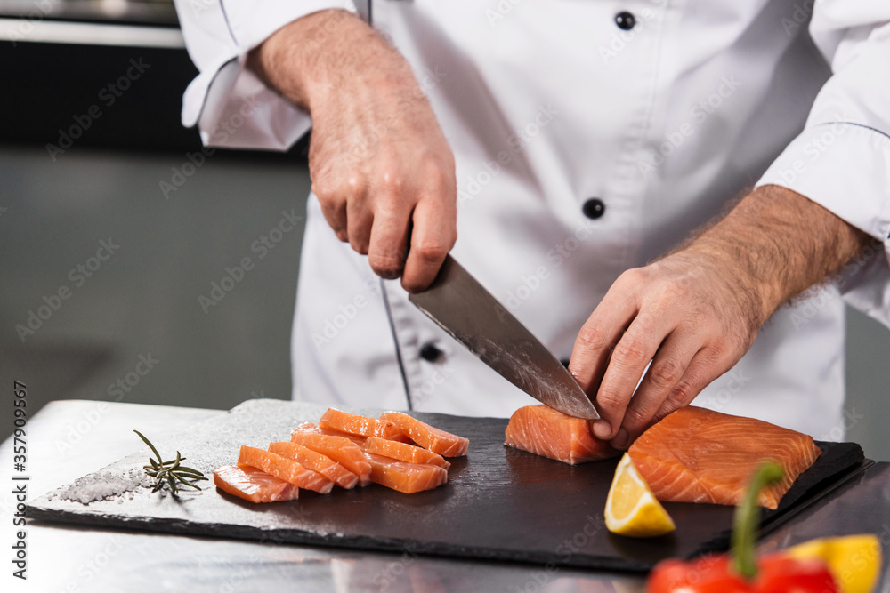 Chef male cutting fish fillet. Closeup chef hands slice salmon at kitchen table.