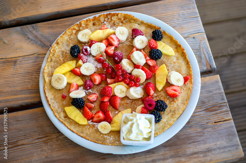 Large pancake with fresh summer fruit and whipped cream on a wooden table. Top view.