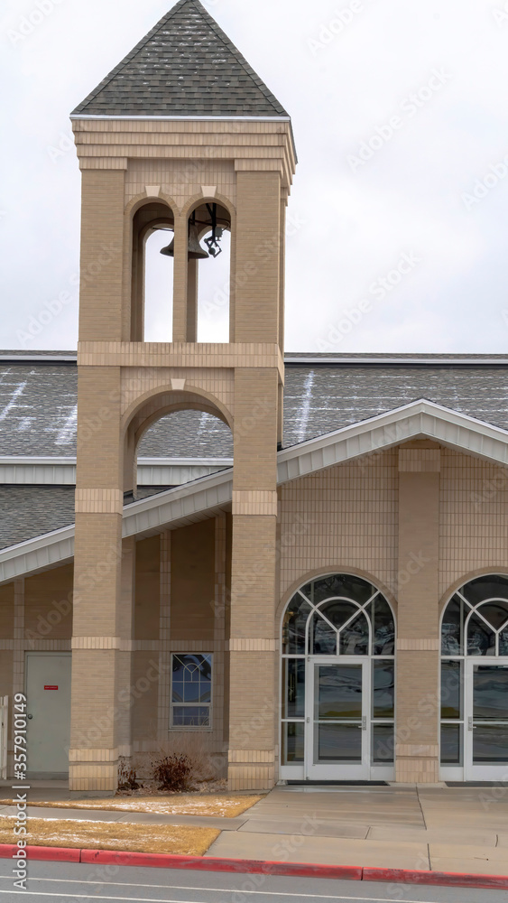 Vertical Church facade with glass front doors and modern belfry tower against cloudy sky