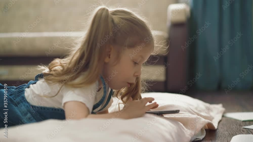 cu, tracking: little girl, beautiful, in blue sundress, with long pigtails, lies on floor and works on smartphone, child swipe, tap on screen, closeup cu, tracking: little girl, beautiful, in blue sundress, with long pigtails, lies on floor and works on smartphone, child swipe, tap on screen, closeup