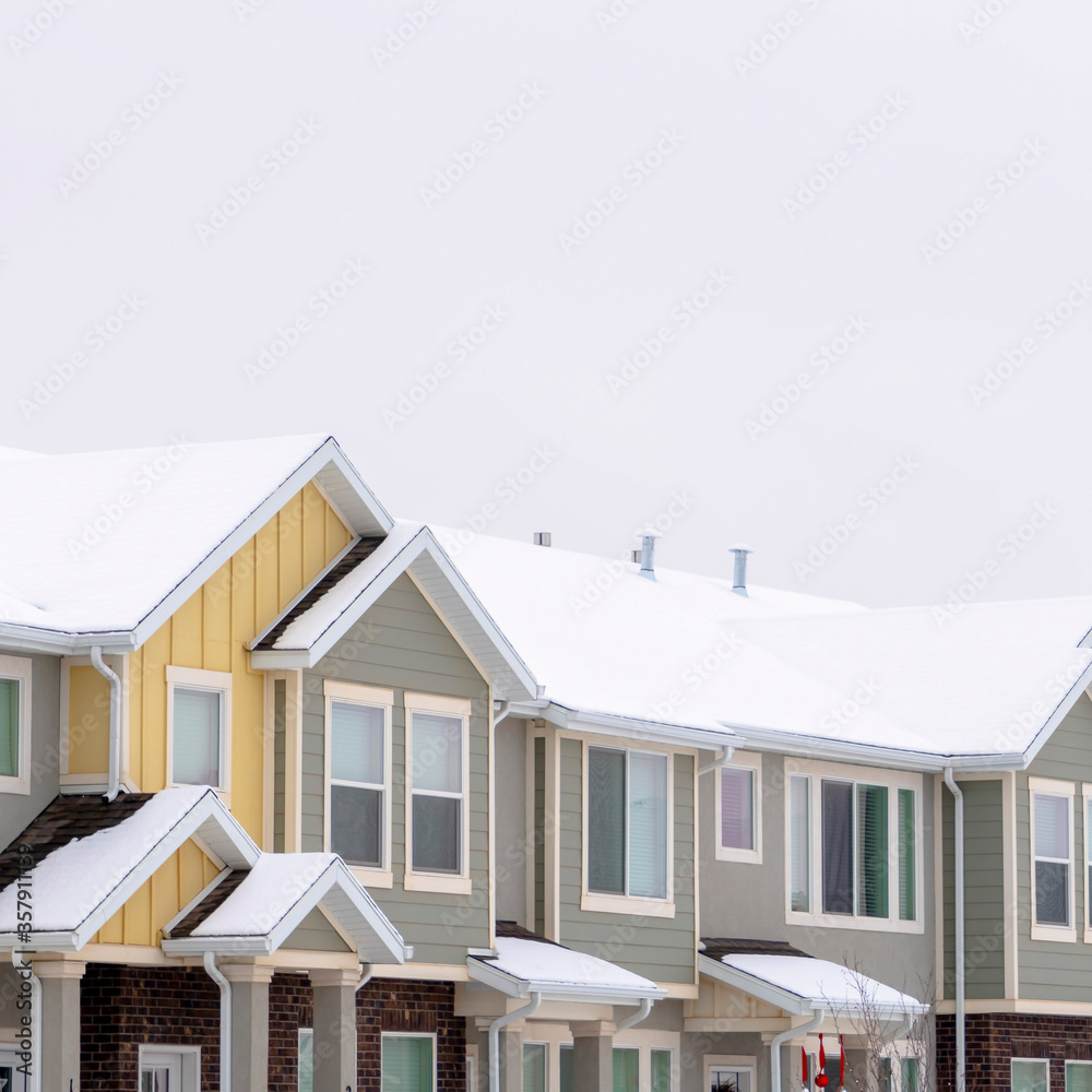 Square frame Facade of townhomes with snow covered pitched and valley roof against cloudy sky