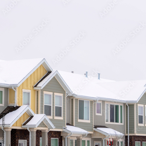 Square frame Facade of townhomes with snow covered pitched and valley roof against cloudy sky © Jason