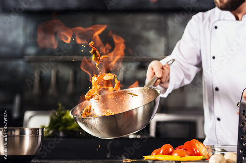 Chef hands keep wok with fire. Closeup chef hands cook food with fire. photo