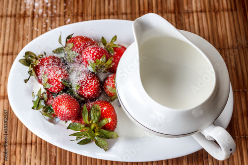 Strawberries sprinkled with sugar on a tray with milk jug