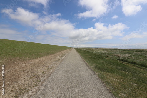 Beautiful wide view over an elongated bicycle path along a dike. Photo was taken on a sunny May day with blue sky and white clouds.