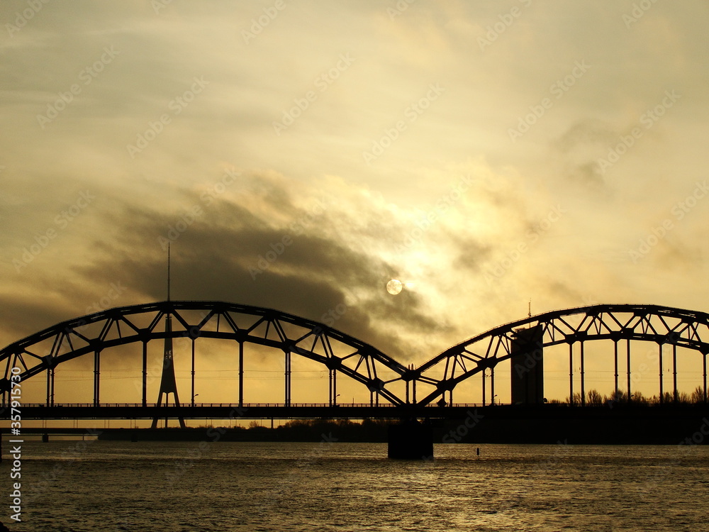 Railway bridge through Daugava in Riga, Latvia. Beautiful view of the big river and sunset though the clouds.