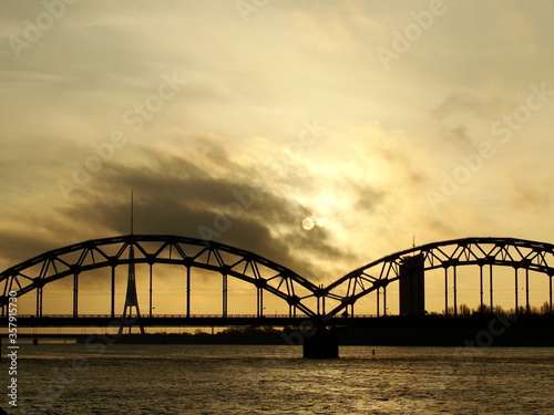 Fototapeta Naklejka Na Ścianę i Meble -  Railway bridge through Daugava in Riga, Latvia. Beautiful view of the big river and sunset though the clouds.