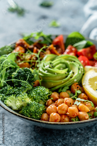 Buddha bowl salad with baked sweet potatoes  chickpeas  broccoli  tomatoes  greens  avocado  pea sprouts on light blue background with napkin. Healthy vegan food  clean eating  dieting  close up