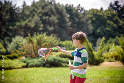 Little boy playing with his soap bubbles toy in the park. Child activity. Springtime concept