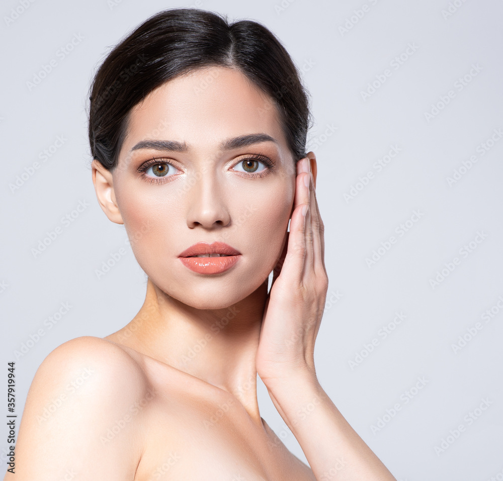 Fototapeta premium Portrait of beautiful brunette girl which touching her fresh face. Beautiful face of young woman with health fresh skin. Beautiful face of young adult woman with clean fresh skin. Skin care.