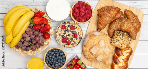 Breakfast Served in the morning with Butter croissant and corn flakes Whole grains and raisins with milk in cups and Strawberry, Blueberry, Raspberry, Kiwi, Fresh Orange Juice on the breakfast table.