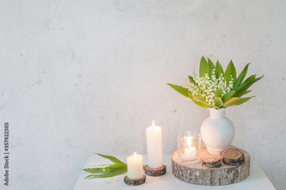 lily of the valley in vase with candles on background old white wall