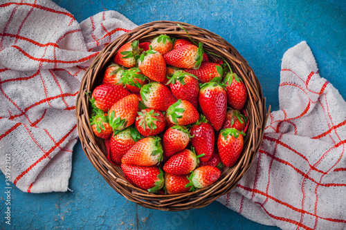 Strawberries fresh overhead colorful arrangement in woven basket on red and white kitchen cloth and rustic blue table studio shot