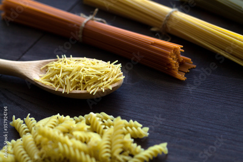 raw pasta on a wooden table. uncooked wheat and tomato spaghetti, fusilli, penne on a dark background with copy space. Italian Cuisine