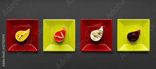 Cakes of various flavors and colors lined up on a black backgroundCakes of various flavors and colors lined up on a black background and on colored square plates photo