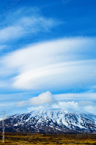 Volcanic land, snowy mountains and meadow and amazing clouds