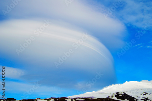Interesting shaped clouds, snowy volcanic mountain in a sunny day