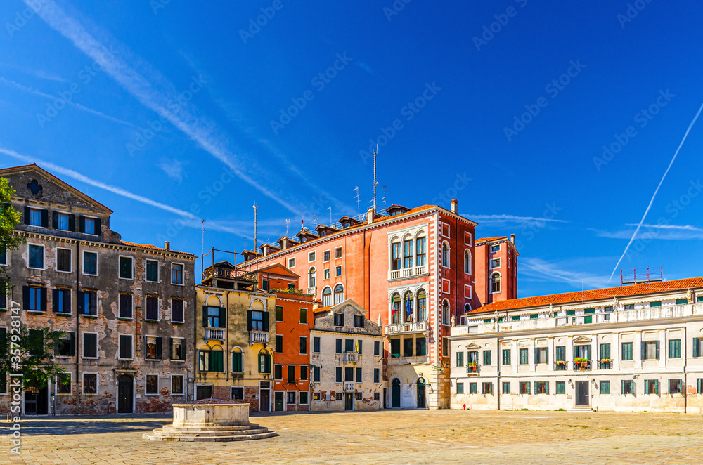 Palace buildings and stone well on Campo San Polo square in Venice historical city centre, blue sky background in summer day, Veneto Region, Northern Italy