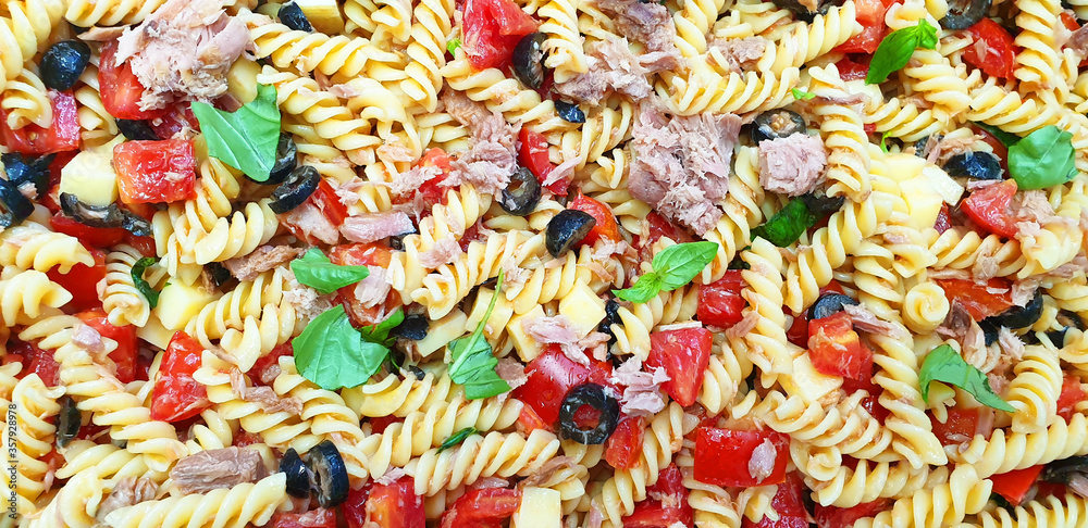 Italian salad: cold pasta, chopped tomatoes, black olives, tuna slices, basil drizzled with olive oil. Italian pasta with fish.