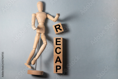 Recap word from wooden blocks on blue grey desk with wwoden figure person