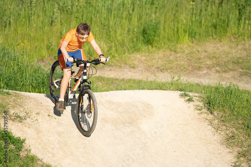 Boy in sunglasses riding a bicycle from a hillock
