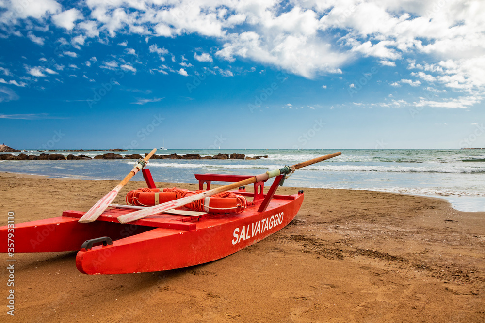 Typical red rescue boat, with oars, used by Italian lifeguards, stationary on the sand. 