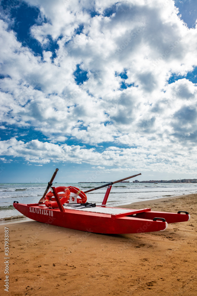 Typical red rescue boat, with oars, used by Italian lifeguards, stationary on the sand. 