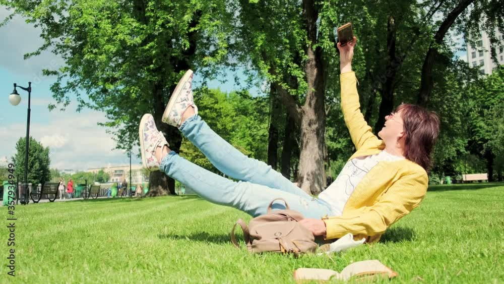 Pretty red-haired attractive caucasian woman makes selfie photos on smartphone for social networks at park on sunny spring day. 2x slow motion, UHD 4K video.