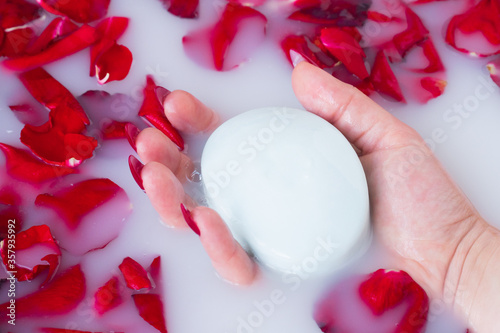 Female hand hold soap against the background of milk or white water with rose petals