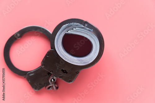 twisted wad of dollars buttoned with handcuffs on a pink background