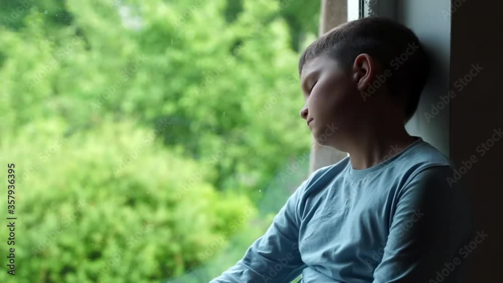 child kid sitting on the window sill looking on green trees. summer landscape. bored, alone sad sick boy wants to go outdoor to play with friend on vacation.home quarantine isolation. social distance. child kid sitting on the window sill looking on green trees. summer landscape. bored, alone sad sick boy wants to go outdoor to play with friend on vacation.home quarantine isolation. social distance.