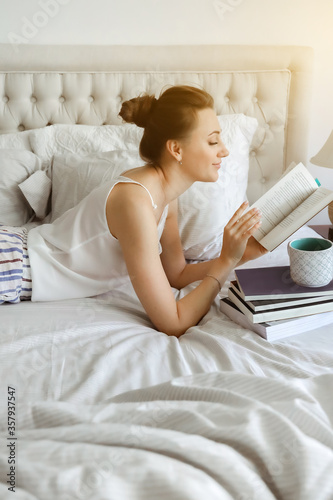 Happy young woomen relaxing on bed and reading book staying at home. Girl learning at home reading literature during quarantine photo