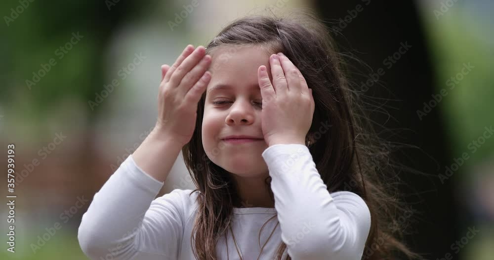 Funny little 6 years girl smiling looking at camera at city, preschool child with stroking himself on the face funny