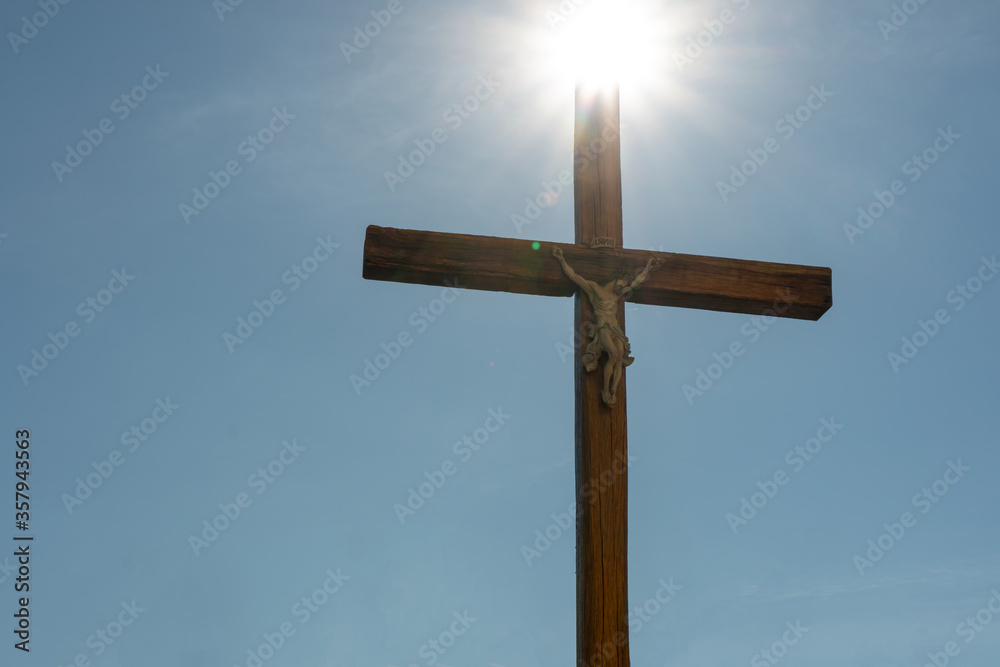 An old wooden Catholic cross against the background of the sun and clear blue sky. Religion and service to God as a path to redemption from sin. The face of Jesus crucified on the cross.