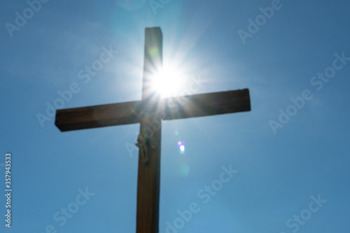 An old wooden Catholic cross against the background of the sun and clear blue sky. Religion and service to God as a path to redemption from sin. The face of Jesus crucified on the cross.
