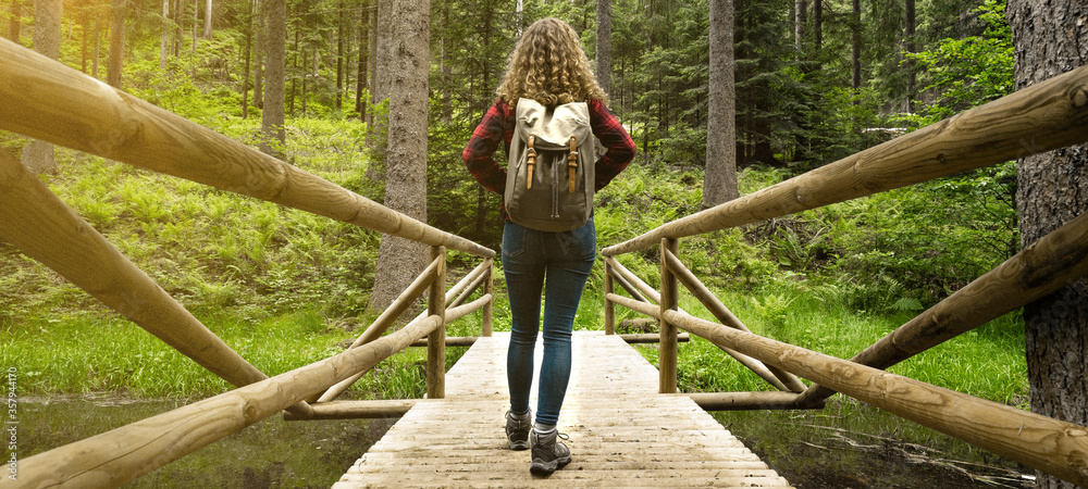 Hiking nature outdoor background - Young pretty girl woman with curly hair and backpack on her back hikes on a bridge in the forest (Black Forest Germany)