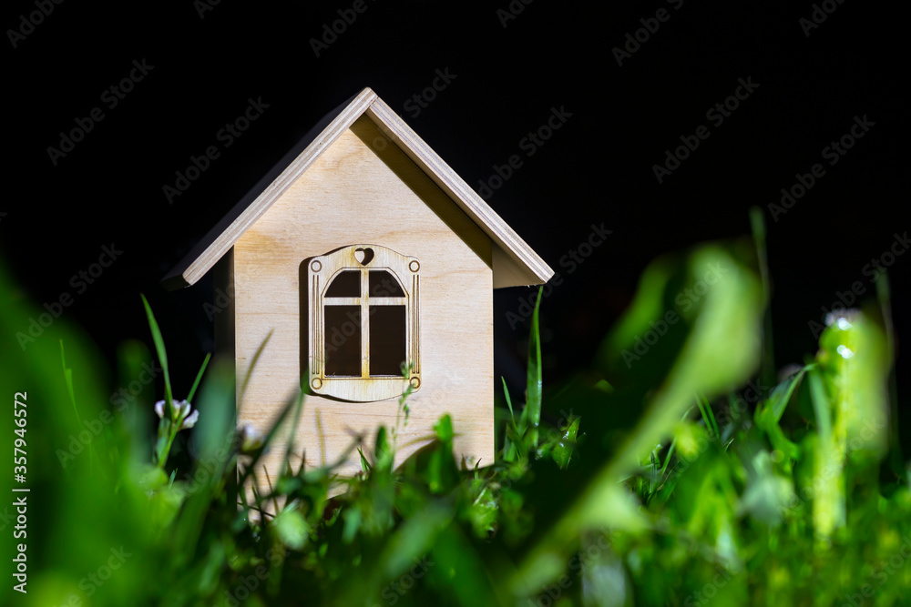night. A toy house made of wood stands on the green grass. Close-up night. A toy house made of wood stands on the green grass. Close-up