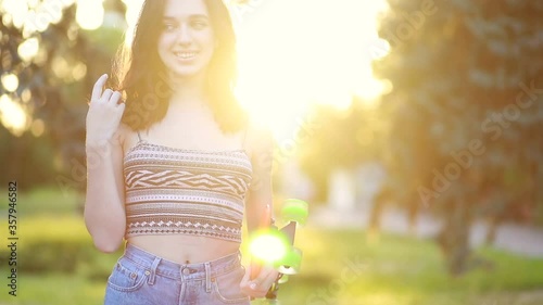 sport, lifestyle, Extreme and people concept - Beautiful girl on the road in the city in sunny weather. Portrait hipster girl smiling with a longboard at sunset. Slow motion photo