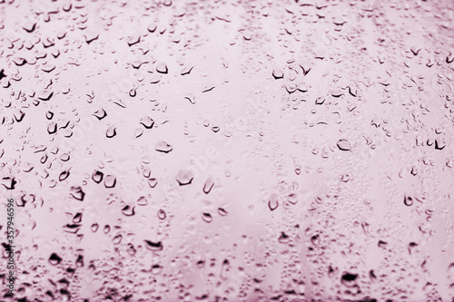 High contrast photo of drops of rain on a window glass with light red scarlet color