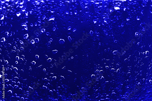 High contrast photo of drops of rain on a window glass with vivid navy blue color