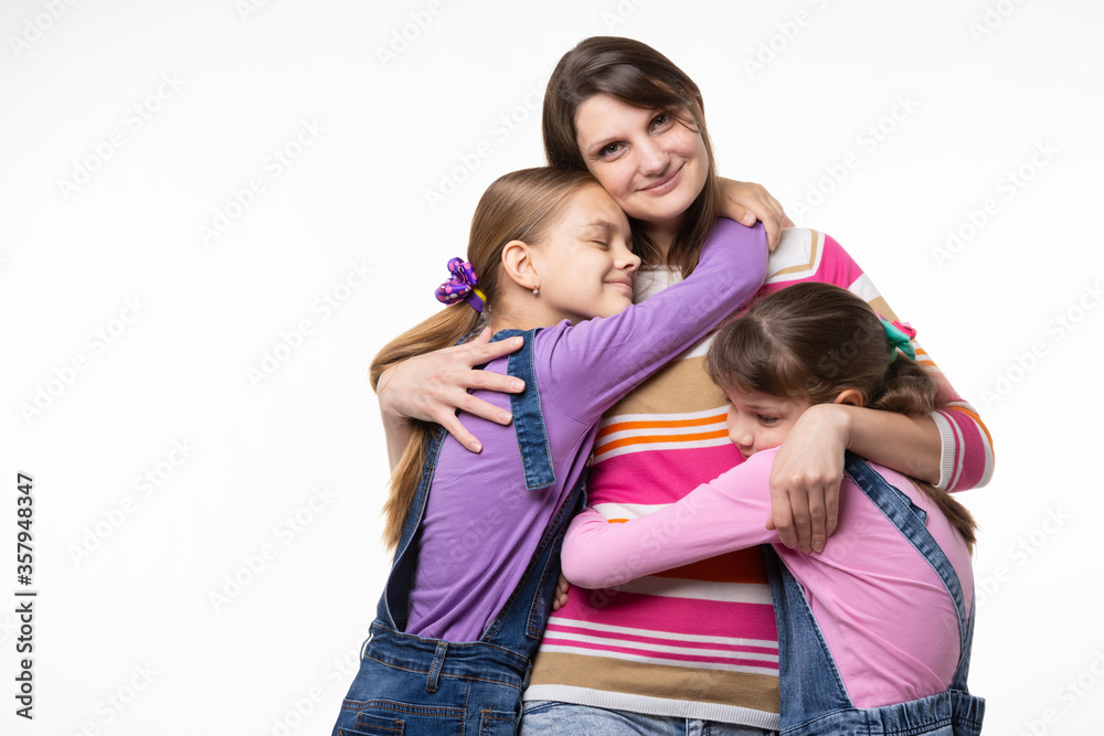 Children hug their beloved mom, mom happily looks in the frame Children hug their beloved mom, mom happily looks in the frame
